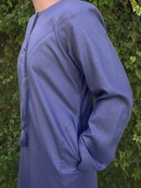 Person wearing a blue thobe against a green leafy background